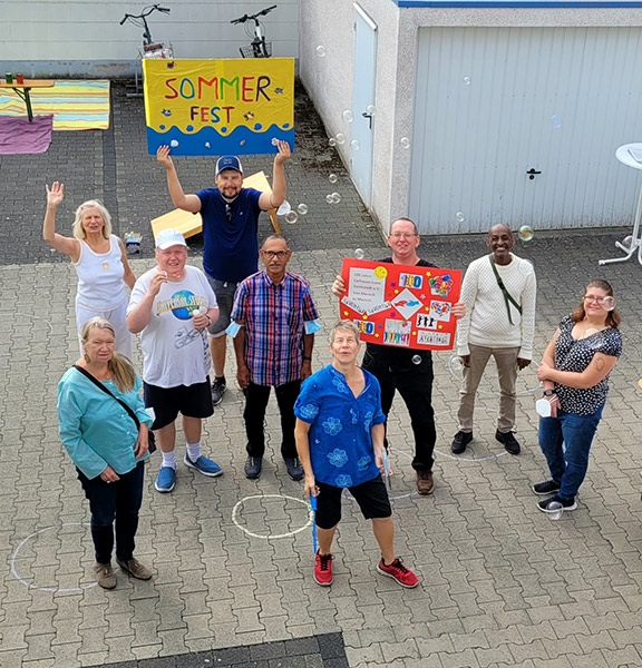 Gruppenbild aus 4 Frauen und 5 Männern, die Schilder Hochhalten, eines mit den Aufschrift  „Sommerfest“ und eines mit 100 Jahre Caritasverband Darmstadt (Caritasverband Darmstadt e. V.)