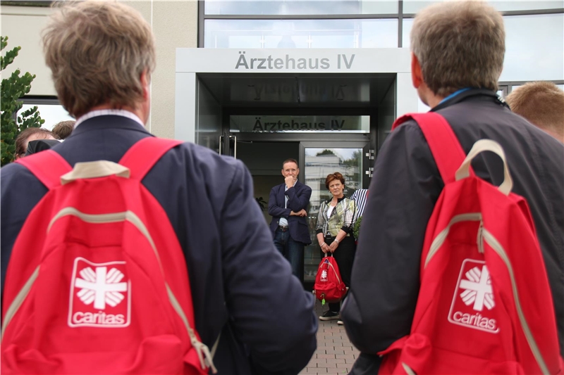 auf dem Bild stehen mehrere Tourteilnehmer mit rotem Rucksack vor einem Krankenhauseingang