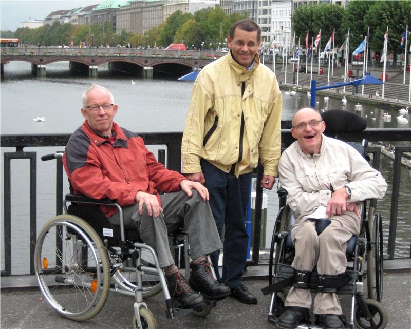 2 Männer im Rollstuhl und 1 Mann dazwischen, stehend auf einer Brücke (©caritasverband bocholt)