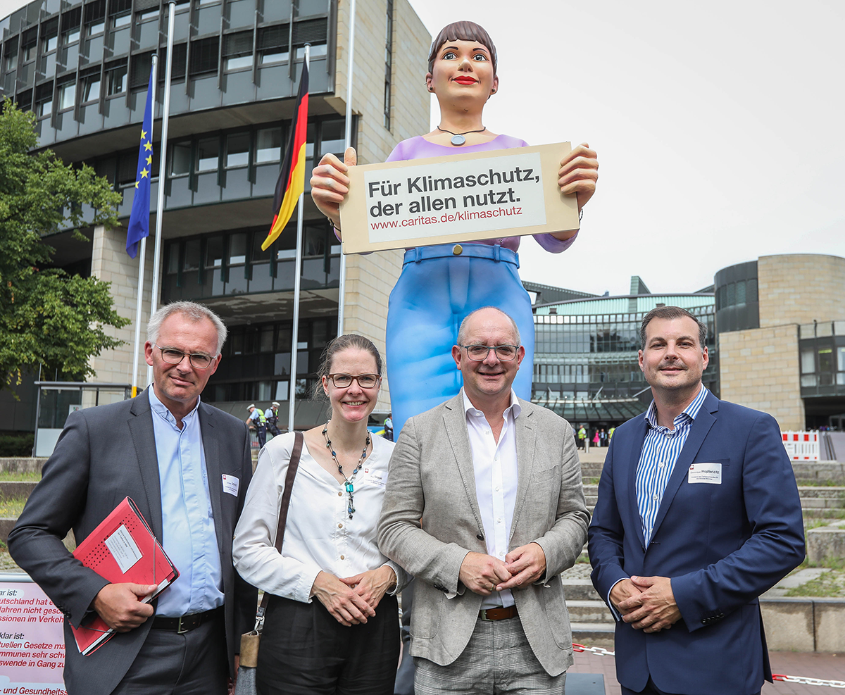 Vier Teilnehmende der Caritas-Kundgebung vor dem Düsseldorfer Landtag, die vor der Figur 'Jenny' stehen (Foto: Hans-Jürgen Bauer)