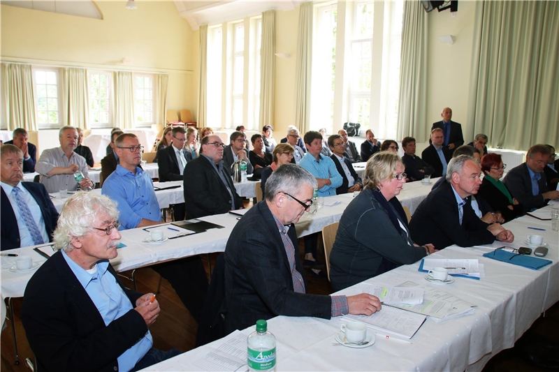 Eine Gruppe von Menschen sitzt auf Stühlen. Die Aufmerksamkeit ist nach vorne gerichtet.