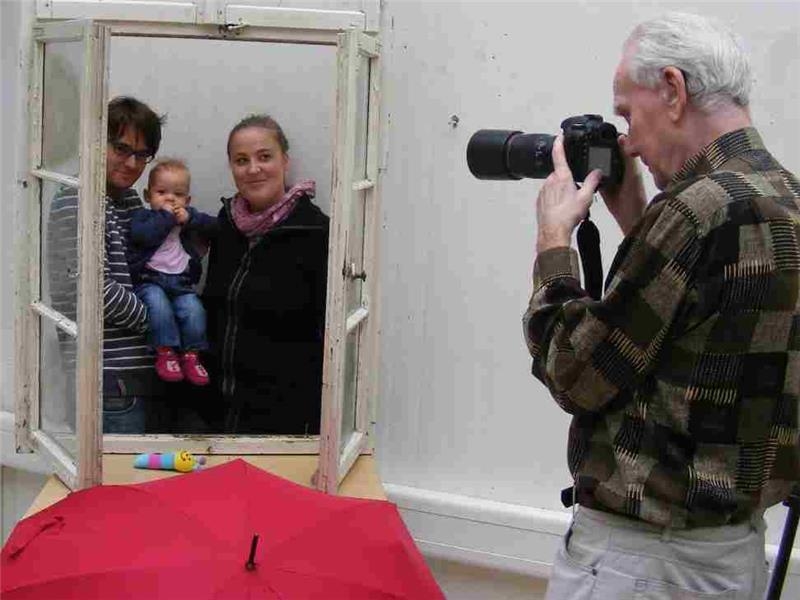 Ein Mitglied der Fotofreunde Bad Kreuznach lichtet eine junge Familie durch ein Fenster hindurch ab. (Caritasverband Rhein-Hunsrück-Nahe)