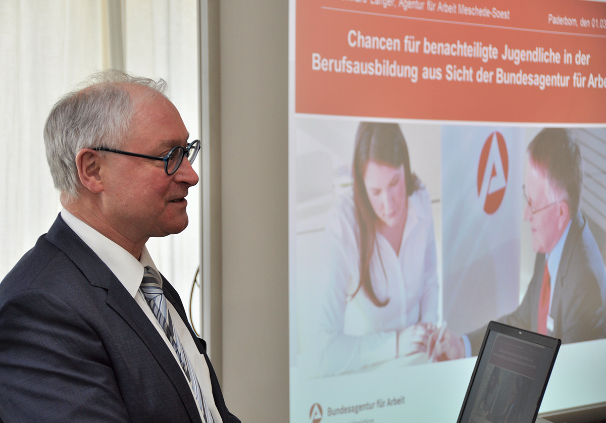 Dr. Reinhard Langer hält bei der Fachtagung 'Lehre statt Leere - Chance Berufsabschluss!' in Paderborn seine Präsentation. Im Hintergrund ist seine Power-Point-Präsentation auf der Leinwand zu sehen (cpd/Jürgen Sauer)