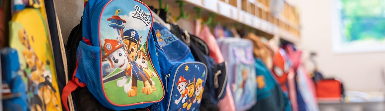 Bunte Kinderrucksäcke hängen an einer Garderobe