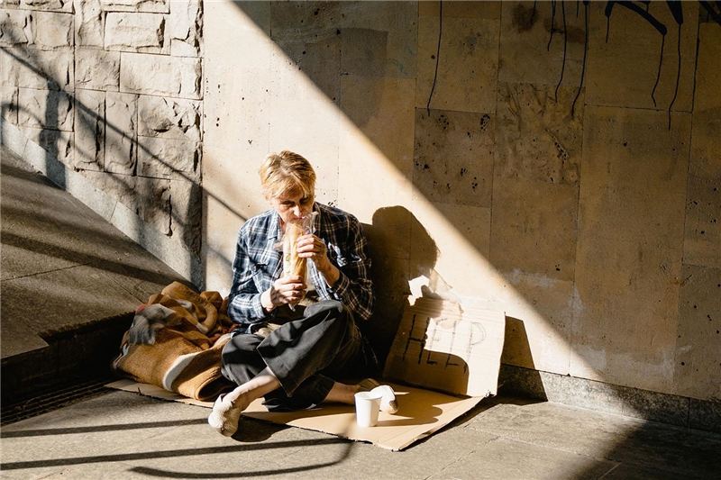 Eine Frau mit kurzen blonden Haaren sitzt auf der Straße und isst ein Brot.