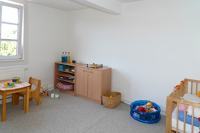 Kinderspielzimmer mit Tischchen und zwei Stühlen, Spielzeugregal, Schrank und Gitterbettchen (Caritasverband Darmstadt e. V. / Jens Berger)