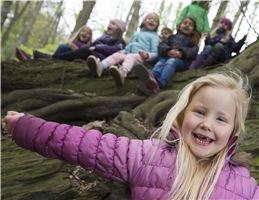 Ein Mädchen breitet lachend vor einem Felsen, auf dem weitere Kinder sitzen, ihre Arme aus / Dietmar Wäsche