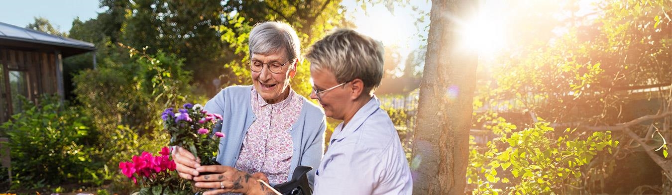 Seniorin und Pflegekraft bepflanzen ein Hochbeet.