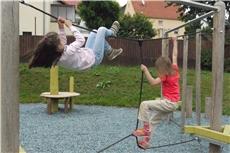 Wir befinden uns auf einem Spielplatz. Ein Mädchen klettert am waagerechten Seil  zur anderen Seite des Kletterturmes. Ein anderes Mädchen balanciert auf einem Seil.