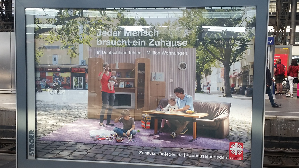 Ein Megalight mit einem Motiv der Caritas-Jahreskampagne 2018 'Jeder Mensch braucht ein Zuhause' auf einem Bahnsteig im Kölner Hauptbahnhof 