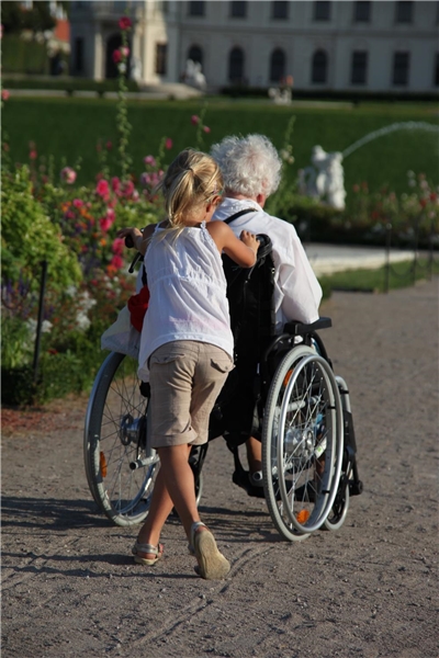 Ein Kind schiebt einen Rollstuhl mit einer alten Dame darin