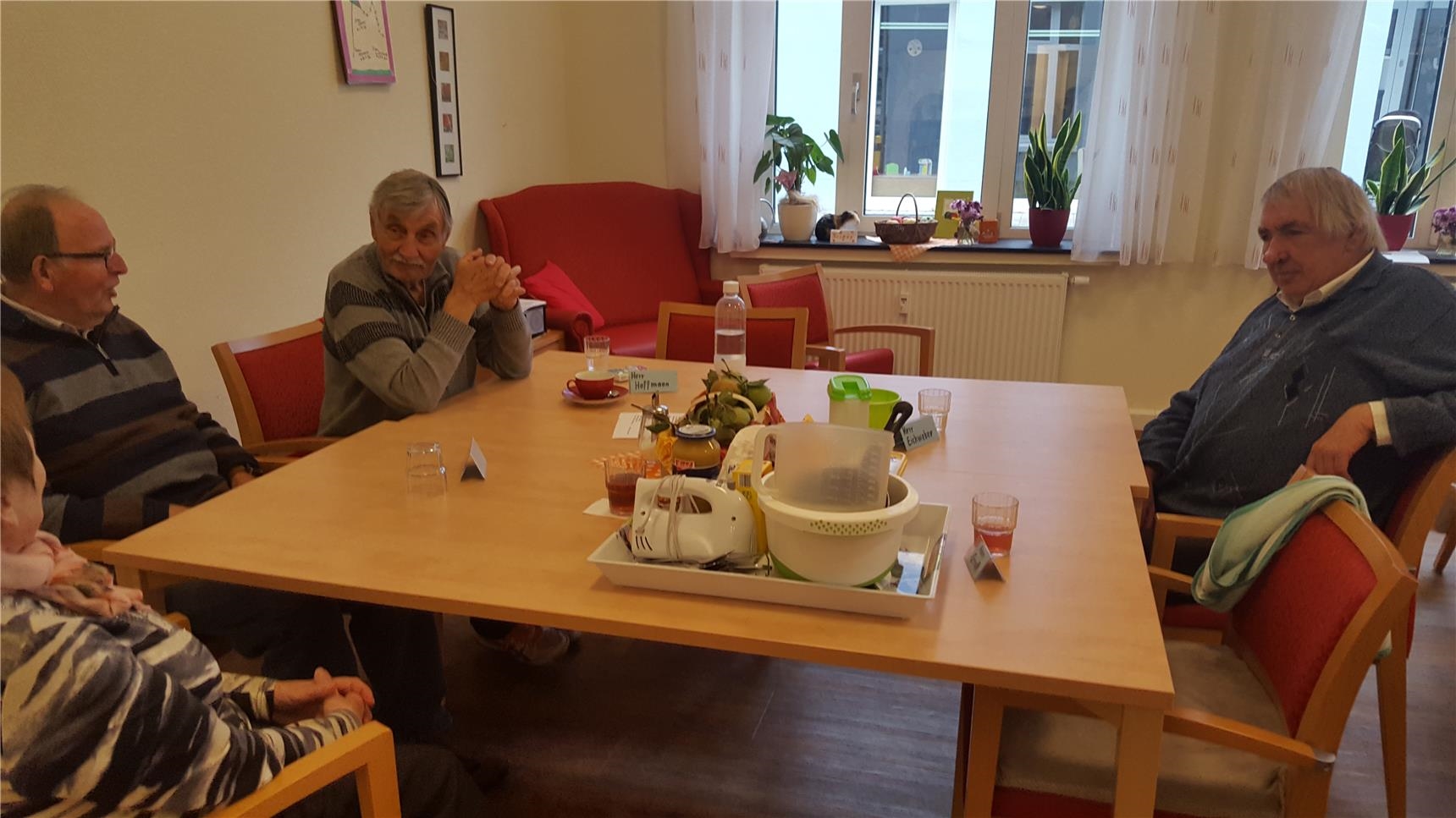 Drei Senioren sitzen am Tisch, auf dem ein Mixer und Schüsseln stehen (Tagespflege St. Rochus)