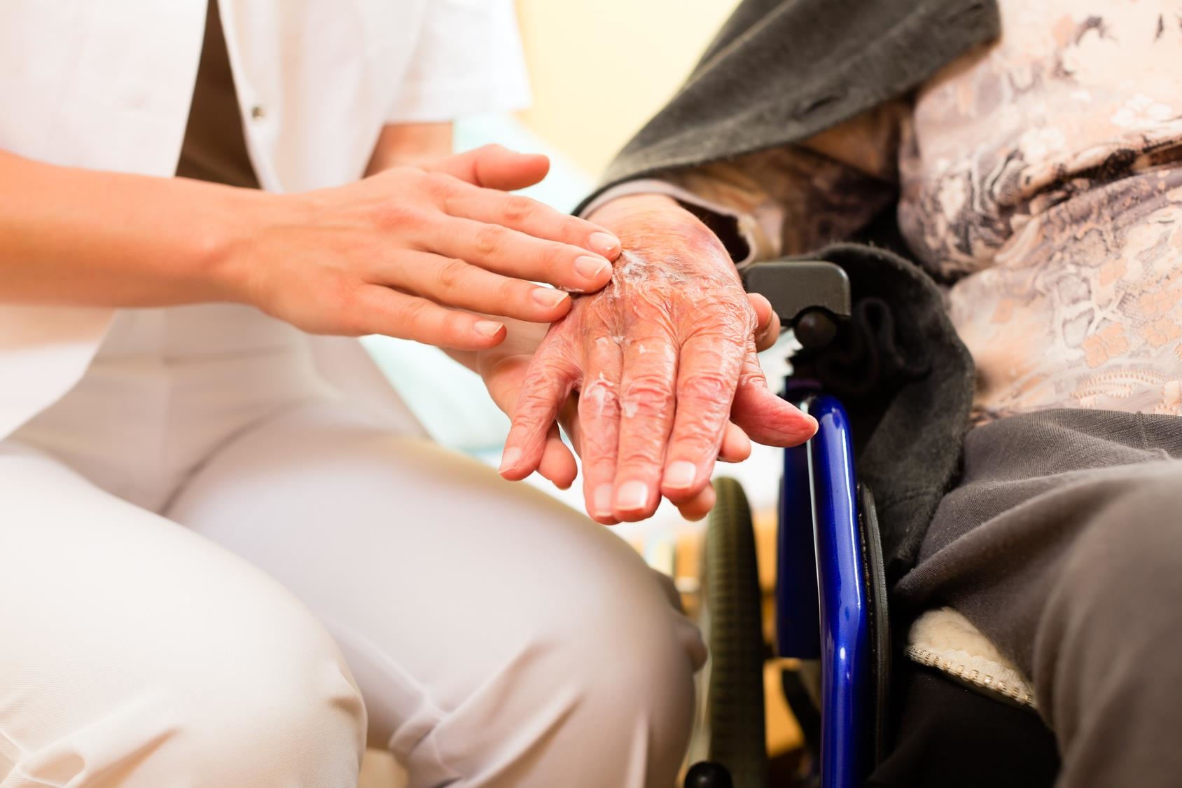 Eine Pflegerin cremt einer Seniorin die Hand ein.