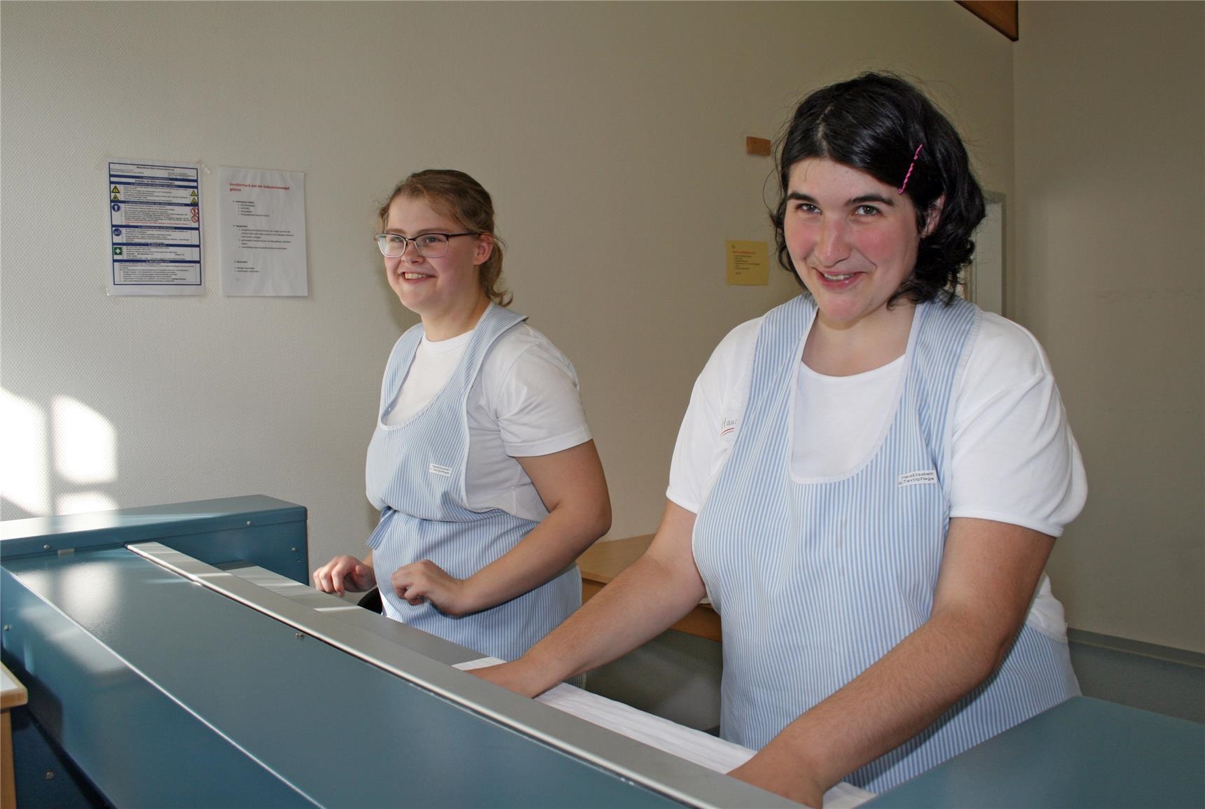 Zwei junge Frauen in Berufskleidung stehen an einer Mangel. (BBZ Haus Elisabeth/Caritasverband Trier)