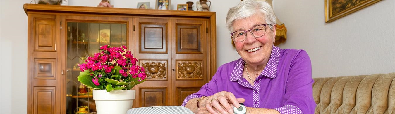 Frau sitzt an einem Tisch auf dem ein Hausnotrufgerät steht.