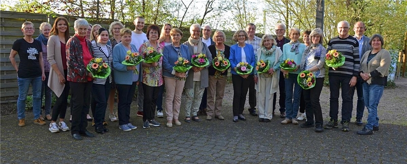 Teilnehmerinnen und Teilnehmer des Frühlingsfestes der Fuldaer Bahnhofsmission sowie die Geehrten, welche einen Blumenstrauß tragen, stehen in einem Garten vor einer Sichtschutzwand