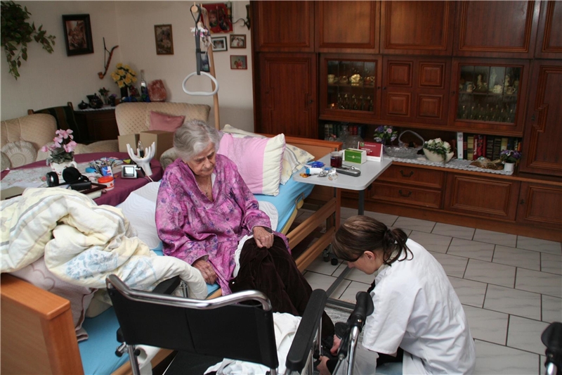 Das Foto zeigt eine Pflegekraft am Bett einer älteren Patientin in ihrer Wohnung.