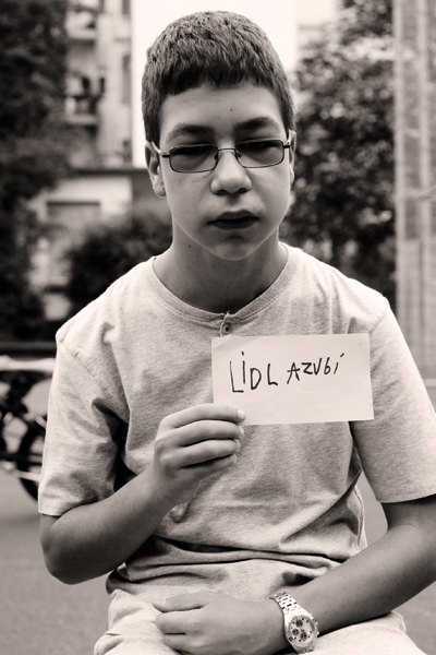 Alexandros (13) auf dem PEV-Platz in Köln. Er hält ein Schild mit der Aufschrift "Lidl Azubi". Die Aufnahme ist in schwarz-weiß.  (Tanja Anlauf (Fotoprojekt „Unsere Zukunft“) )
