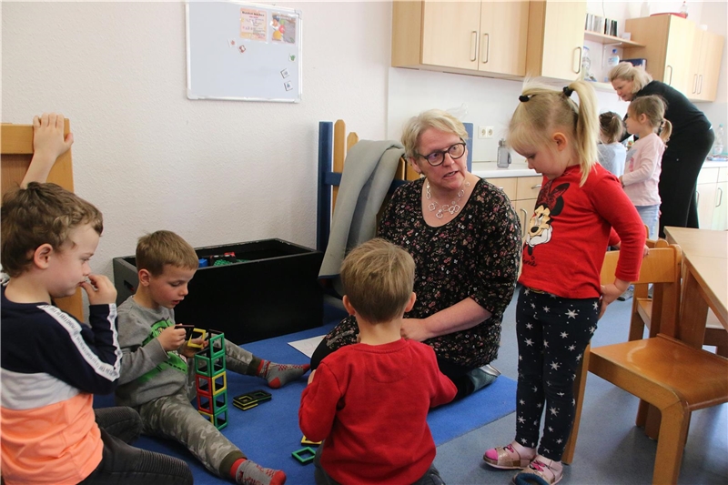 Das Foto zeigt eine Frau, die mit einer Gruppe von Kindern in einer Kita spielt.