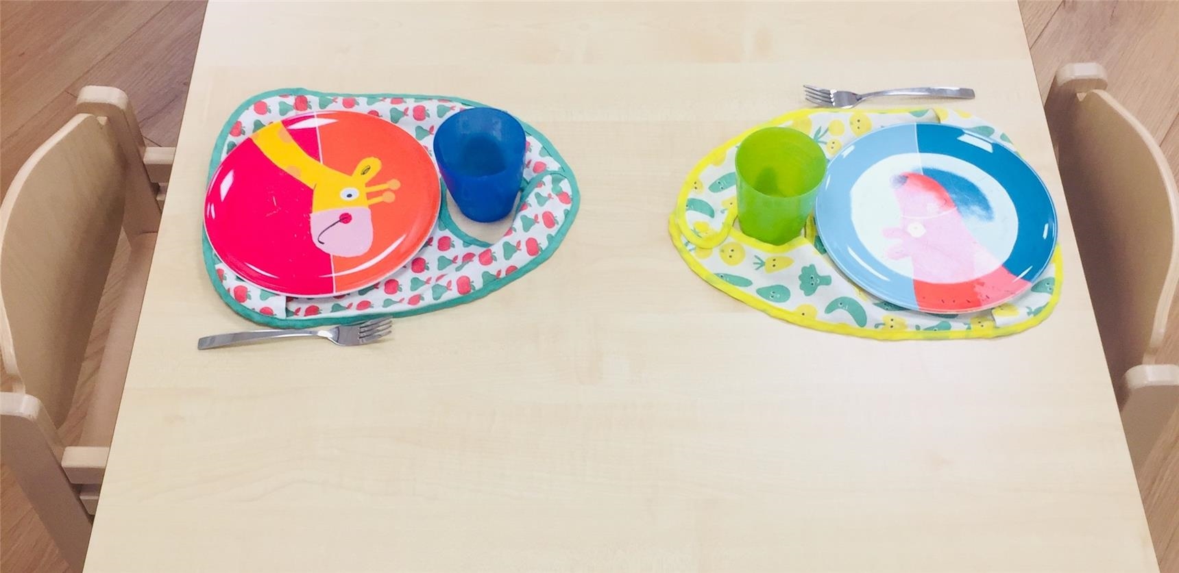 Ein Kindertisch ist gedeckt mit Buntem Geschirr und Kinderlätzchen