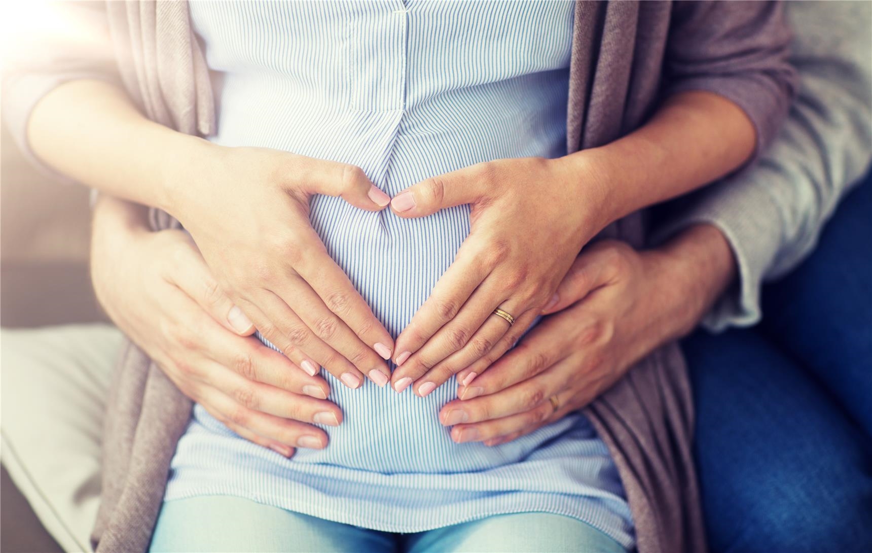 Vier Hände auf Bauch einer schwangeren Frau (AdobeStock_221144515)