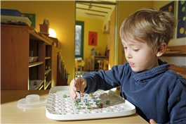 Ein Junge setzt konzentriert mit einer Zuckerzange Glaskugeln auf ein Tablett mit Mulden. / D. Wäsche