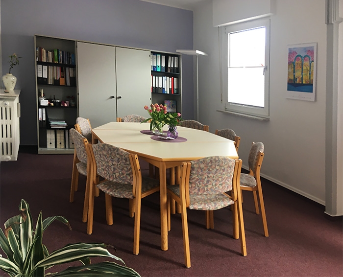 Größerer Büroraum mit Tisch und acht Stühlen. Warmes Ambiente. (Caritasverband Darmstadt e. V.)
