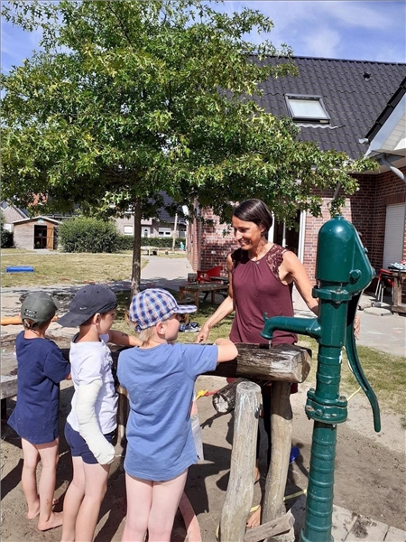 Das Foto zeigt eine Frau und vor ihr an einer Wasserpumpe stehend drei Kinder.