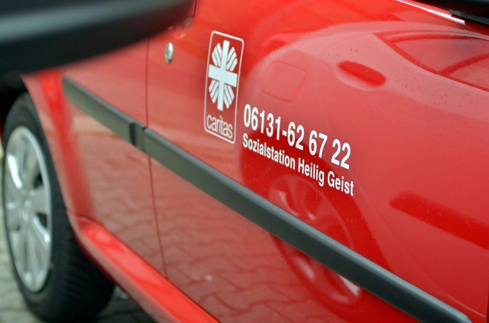 Seitenaufnahme eines roten Autos mit Kontaktdaten der Sozialstation Hl.Geist (Tobias Schneider, taylormade)
