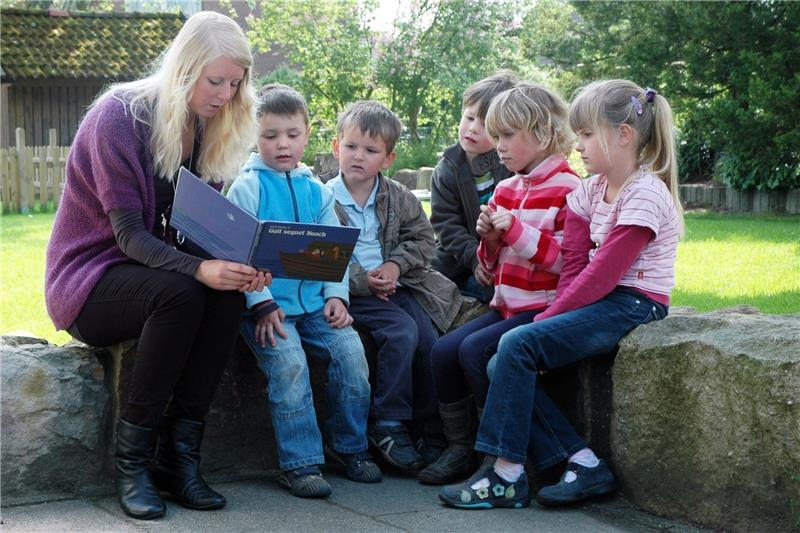 Das Foto zeigt eine Gruppe von Kindern und eine junge Erwachsene, die in einer Reihe auf einer Mauer sitzen.