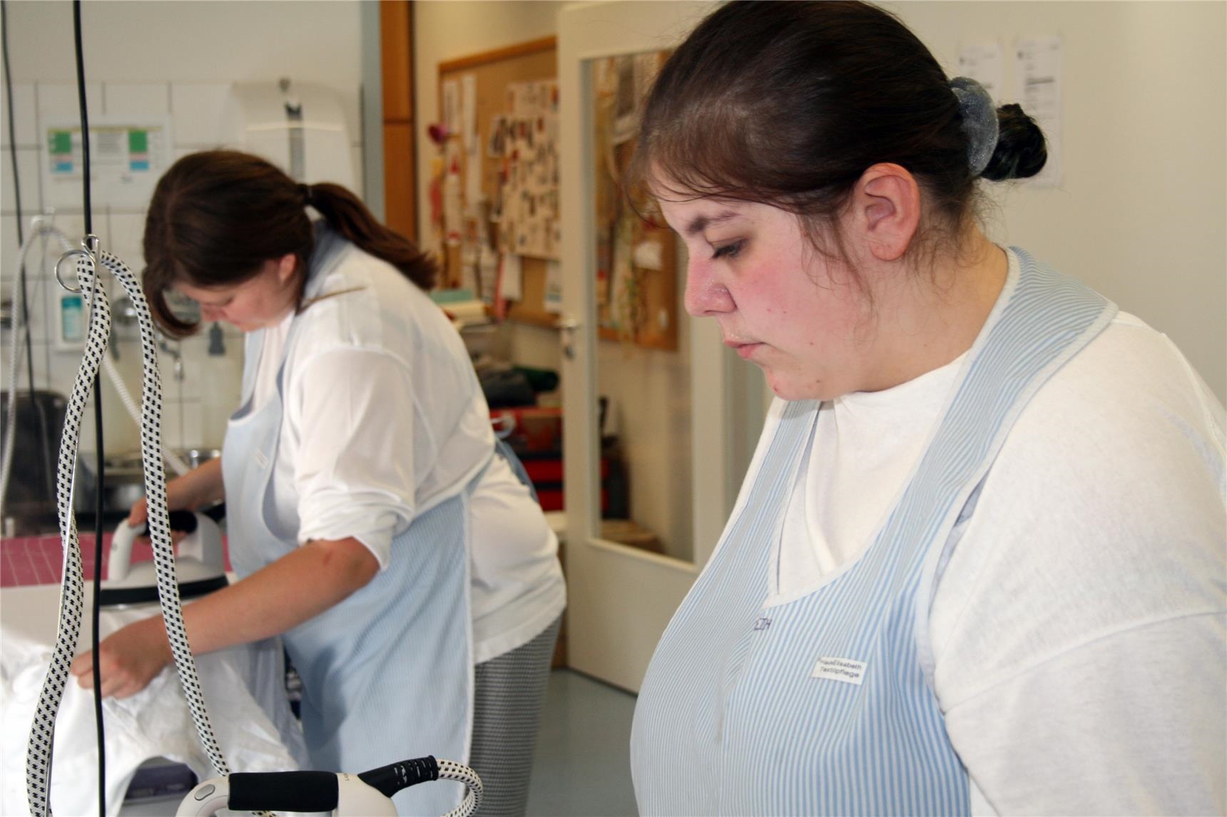 Zwei junge Frauen in Berufskleidung an Bügelbrettern. (BBZ Haus Elisabeth/Caritasverband Trier)