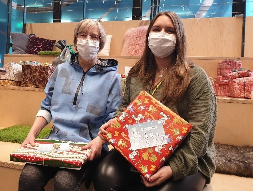 Zwei Frauen sitzen nebeneinander, sie halten bunt verpackte Geschenke in den Händen. 