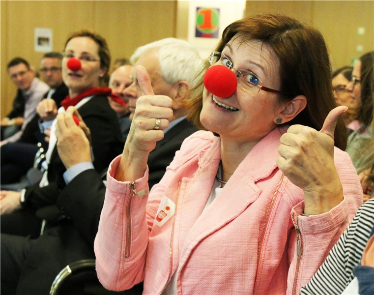 Das Foto zeigt eine Frau, die eine rote Nase aufhat und begeistert in die Kamera schaut.