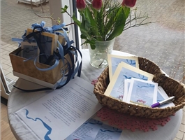 Auf einem ganz in Blau gehaltenen Tisch stehen Karten, ein Frühlingsstrauß, Stifte ein Korb mit blauen Bändern. / Vera Thöne