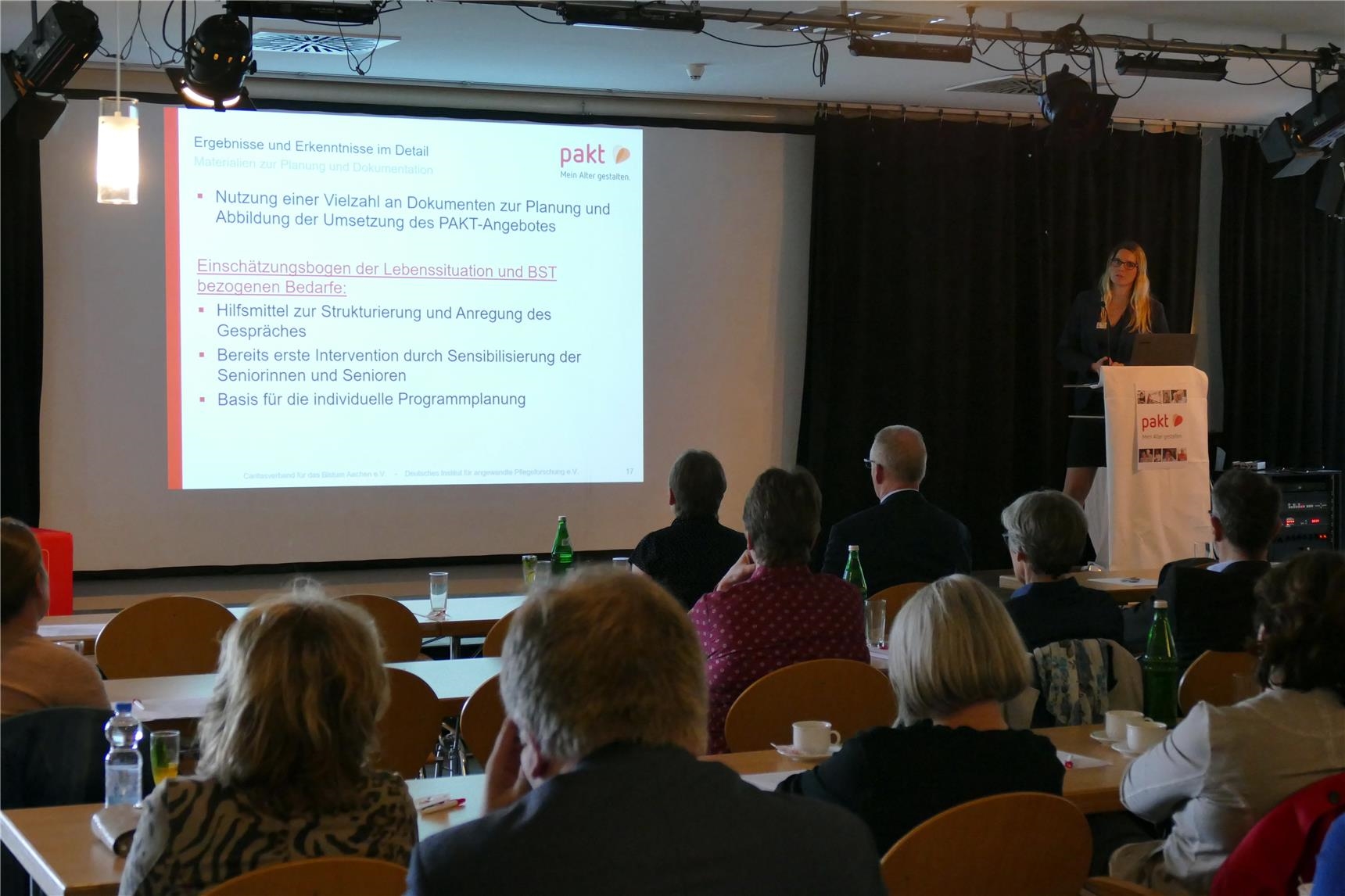 Rednerin am Rednerpult vor schwarzem Hintergrund präsentiert Powerpoint-Präsentation (DiCV Aachen)