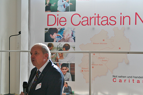 Diözesan-Caritasdirektor Heinz-Josef Kessmann steht einem Handmikrofon auf dem Podium und hält eine Rede. Im Hintergrund ist ein Faltdisplay der Caritas in NRW zu sehen. (Markus Lahrmann)