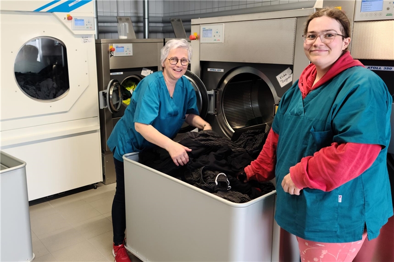 Foto von der Fachkraft Regina Mehren und der Beschäftigten Franziska Drost, die Wäsche aus der Maschine holen