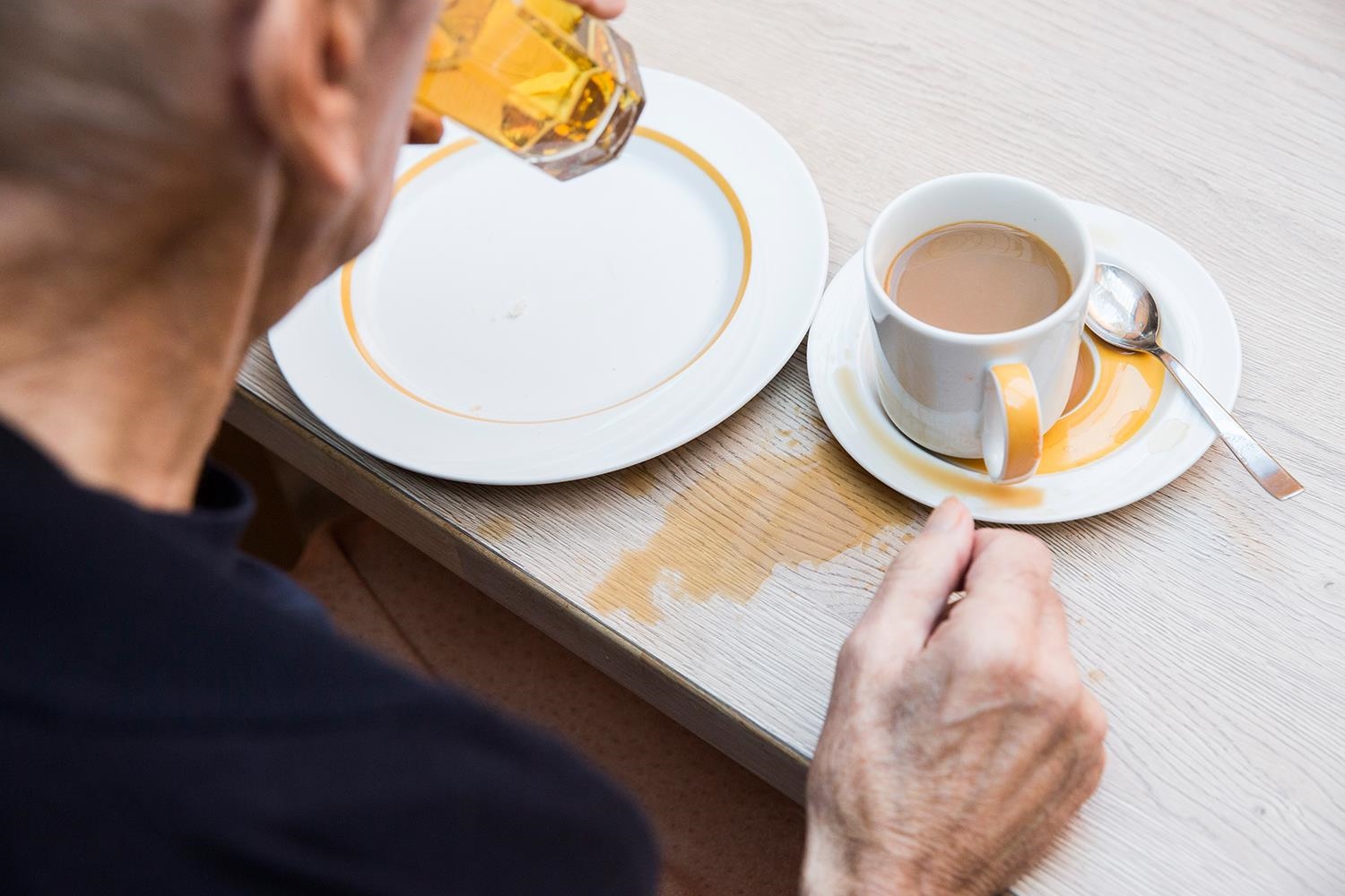 Die Hände eines älteren Menschen neben einer zum Teil verschütteten Tasse mit Kaffee (Deutscher Caritasverband e. V. / Sebastian Pfütze)