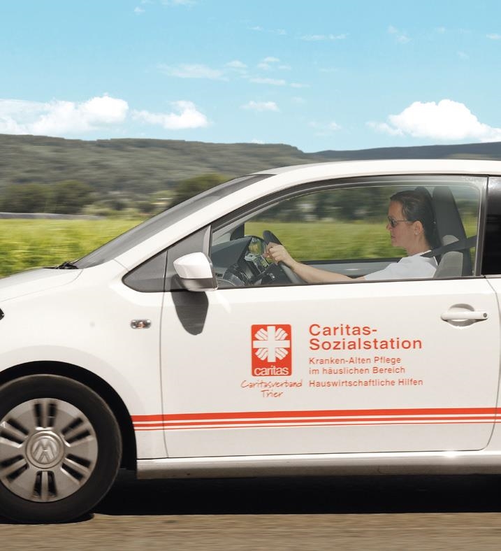Teilansicht eines fahrenden weißen Autos mit der Aufschrift Caritas-Sozialstation; am Steuer eine junge Frau (Caritasverband Trier e. V.)