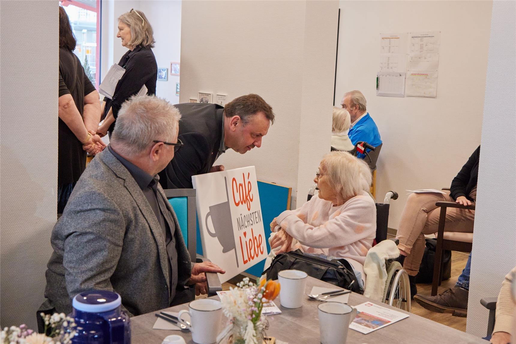 Rainer Lehmler zeigt das Schild Café Nächstenliebe einer Bewohnerin. (Caritasverband Westerwald-Rhein-Lahn e.V. / Olaf Nitz)