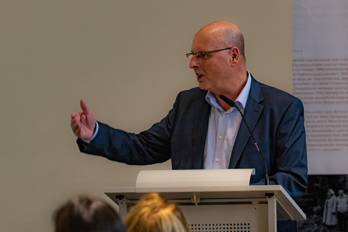 Jörg Rensmann steht bei der CiNW-Fachtagung 'Miteinander Gegeneinander?' in der Alten Synagoge in Essen an einem Pult und hält eine Rede (Foto: © Angelika Kamlage | Caritas in NRW)