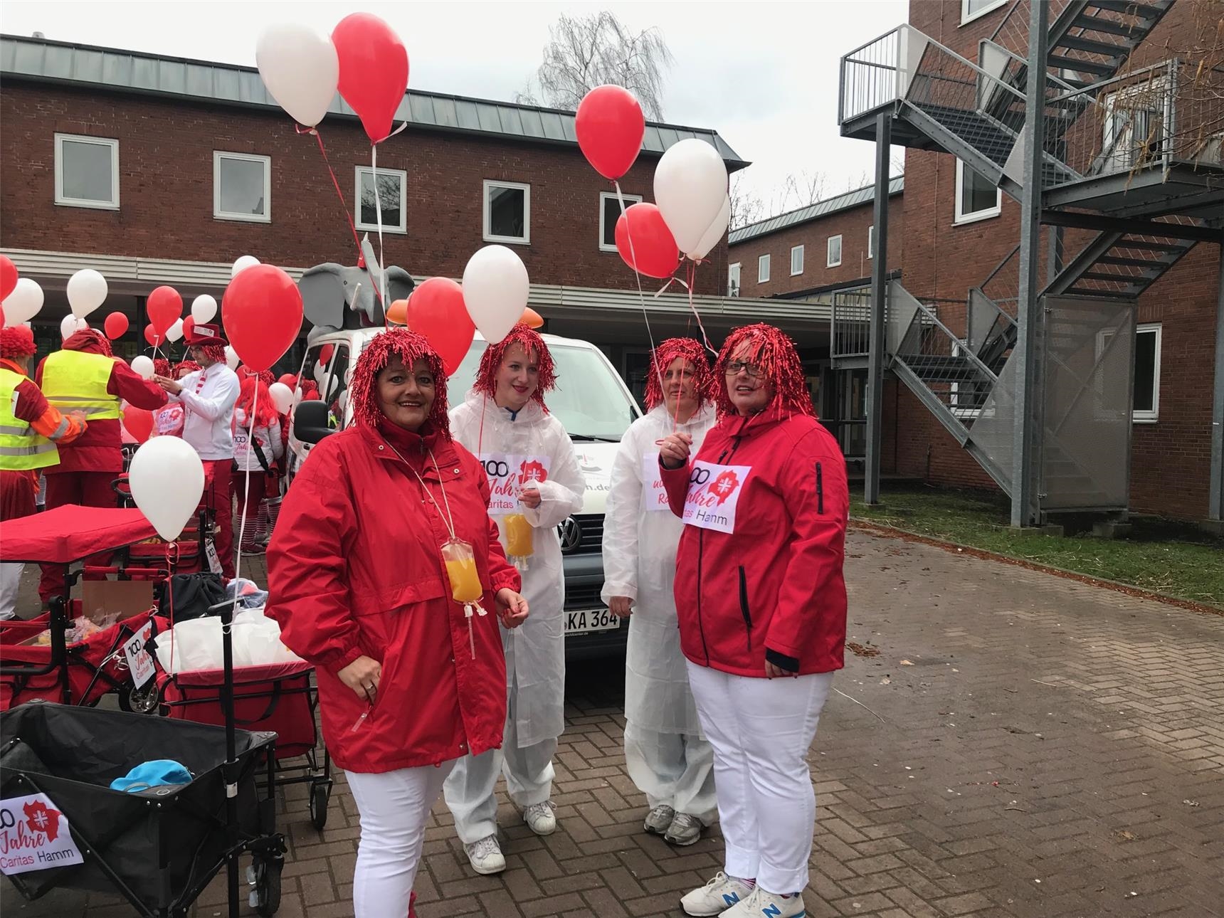 Rot-weiß gekleidete Frauen mit roten Perücken und Luftballons (Caritas Hamm)