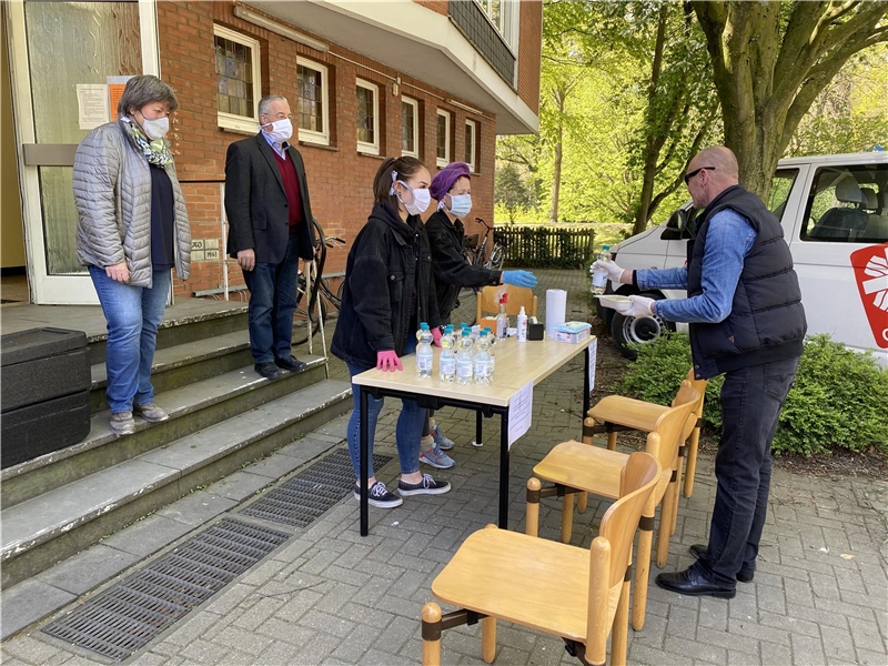 Das Foto zeigt zwei Ehrenamtliche, die an einem Tisch Essen an einen Mann übergeben.