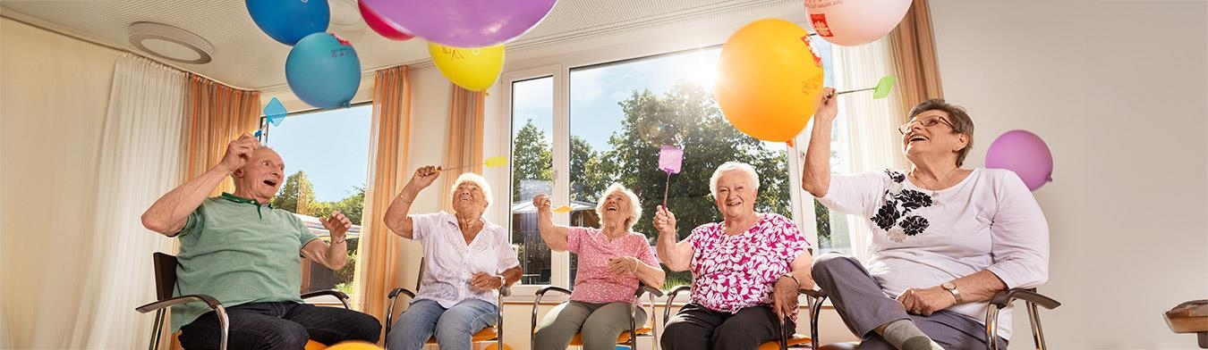 Senior:innen sitzen in einem Kreis und werfen Ballons in die Luft.