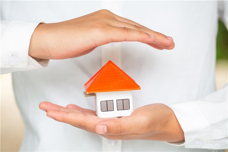Ein Modell eines Hauses in einer Hand, die zweite Hand wird schützend über das Haus gehalten
