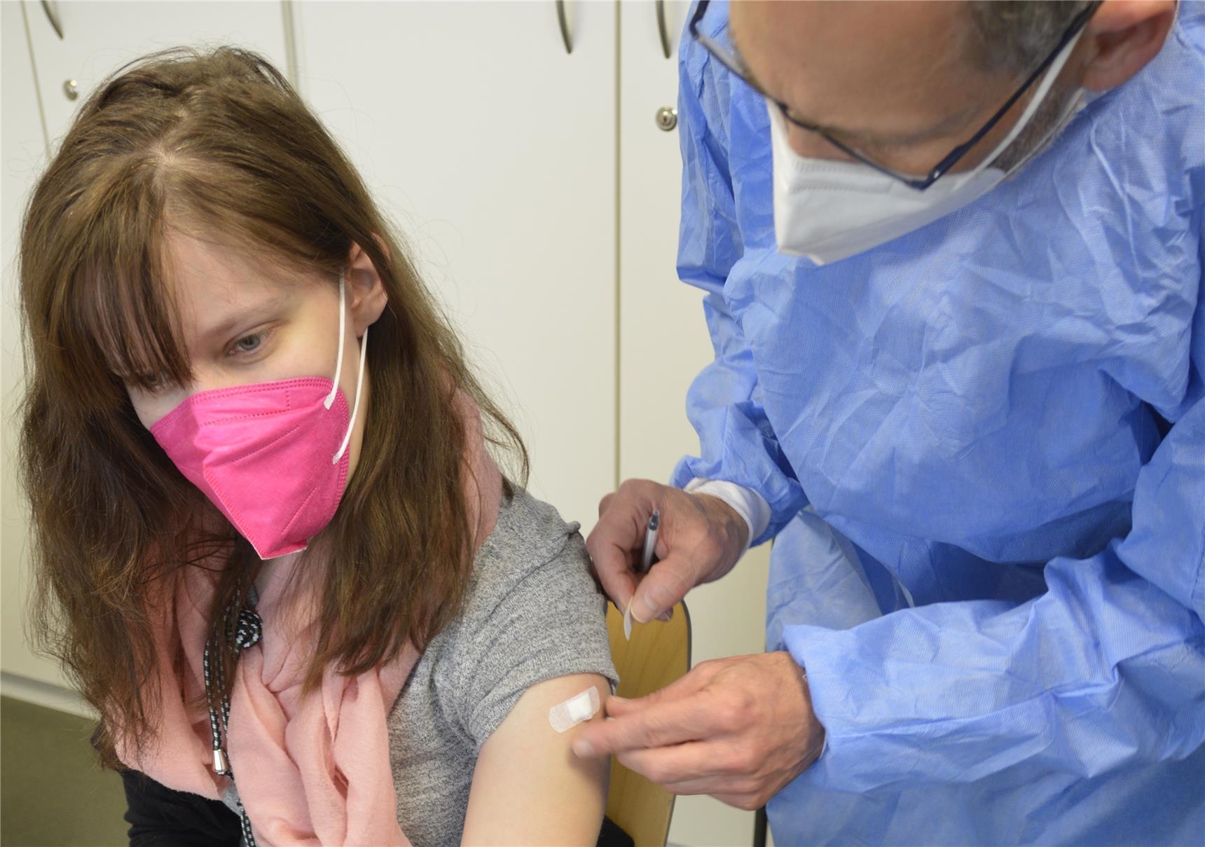 Arzt klebt Pflaster auf Einstichstelle nach Impfung 