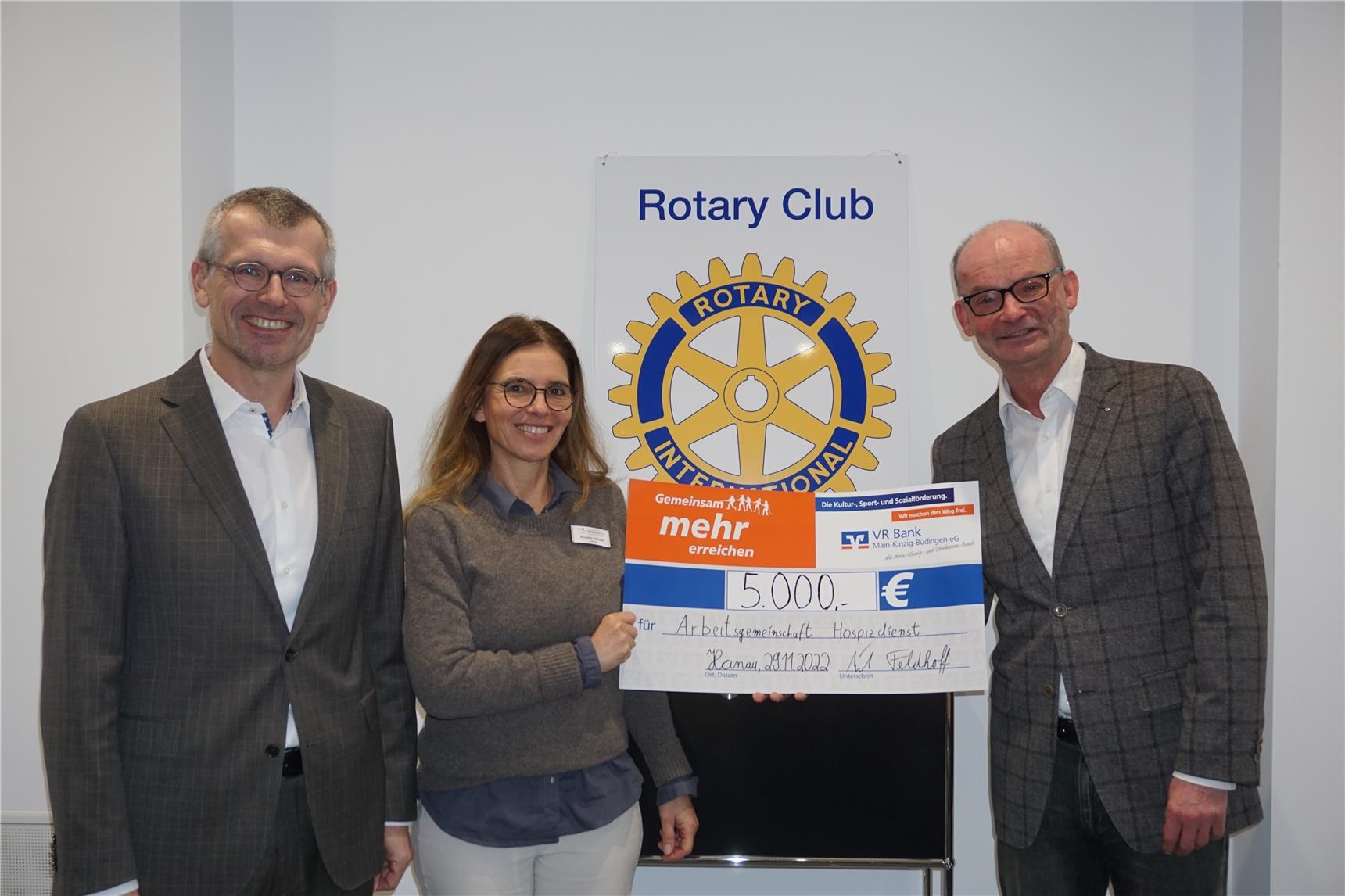 Drei Personen mit einem großen symbolischen Scheck vor dem Logo des Rotary Clubs