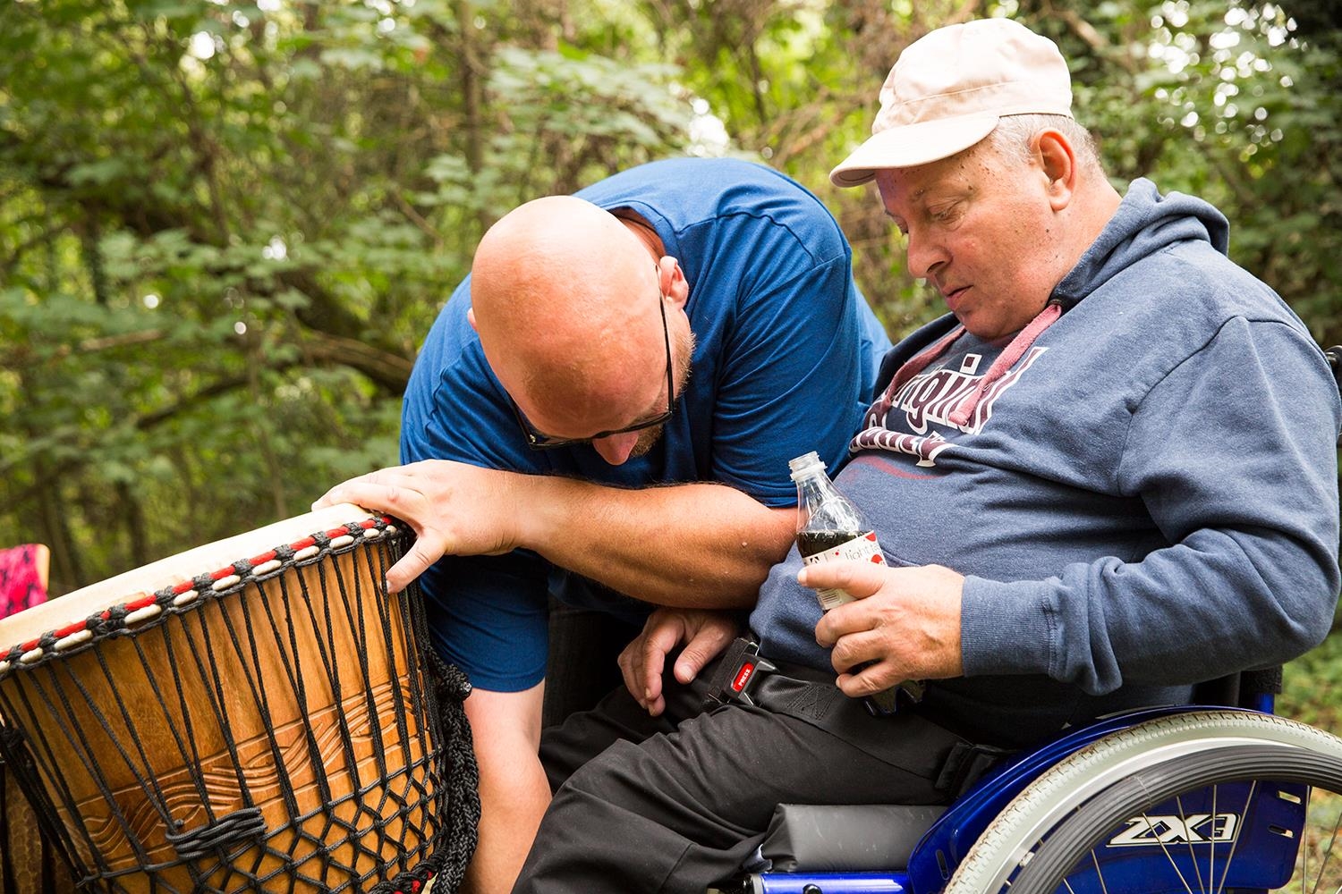 Ein Ehrenamtlicher hilft einem Mann mit Behinderung dabei, eine Trommel vor dessen Rollstuhl zu stellen (Deutscher Caritasverband e. V. / Sebastian Pfütze)