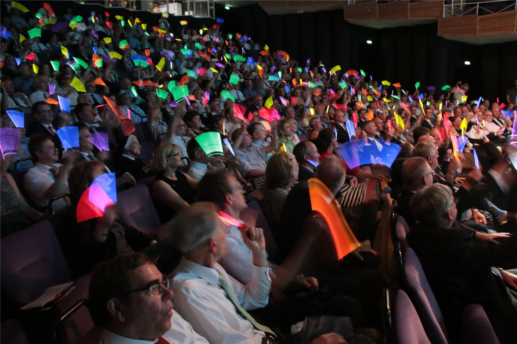 Das Foto zeigt einen vollbesetzten Theatersaal, in dem die Zuschauer Leuchtstäbe schwingen. (Harald Westbeld)