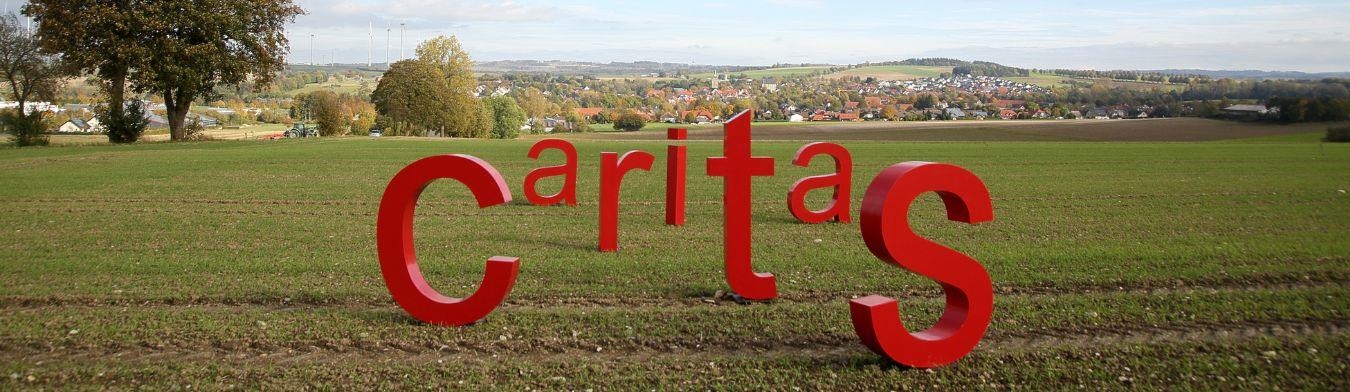 rote Caritas Buchstaben stehen auf Feld mit Blick in die Ferne